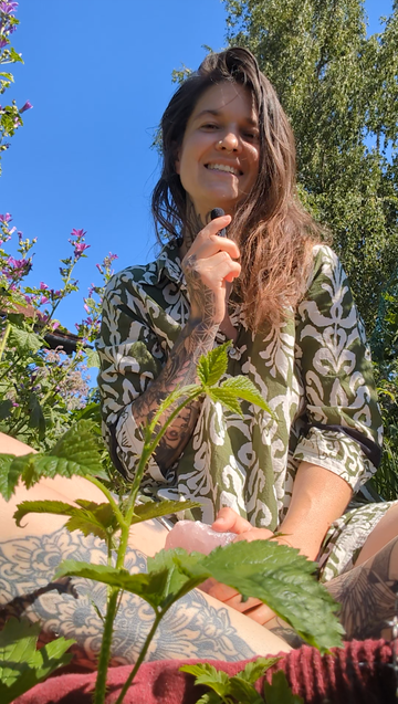 Die Medizinfrau Larissa Llichtermeer sitzt zwischen Blumen und Brombeerranken im Garten